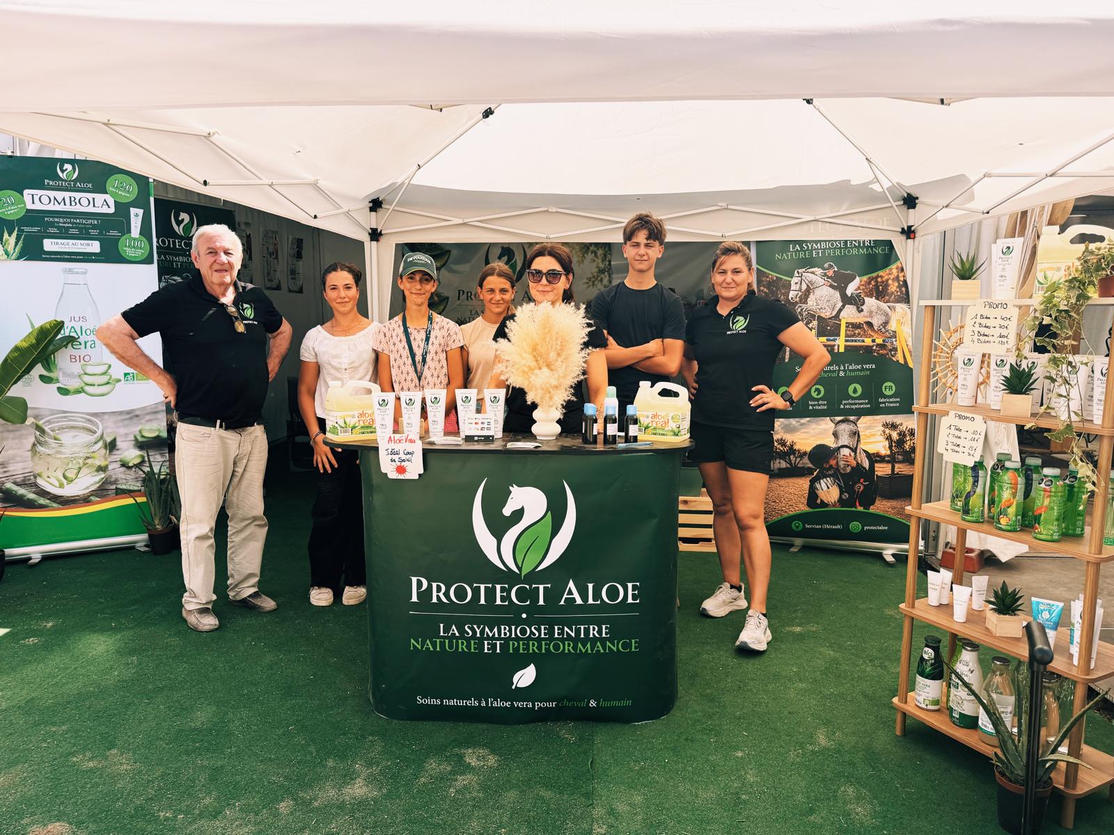 Six personnes de l’équipe derrière le comptoir du stand Protect Aloe, sous une tente blanche