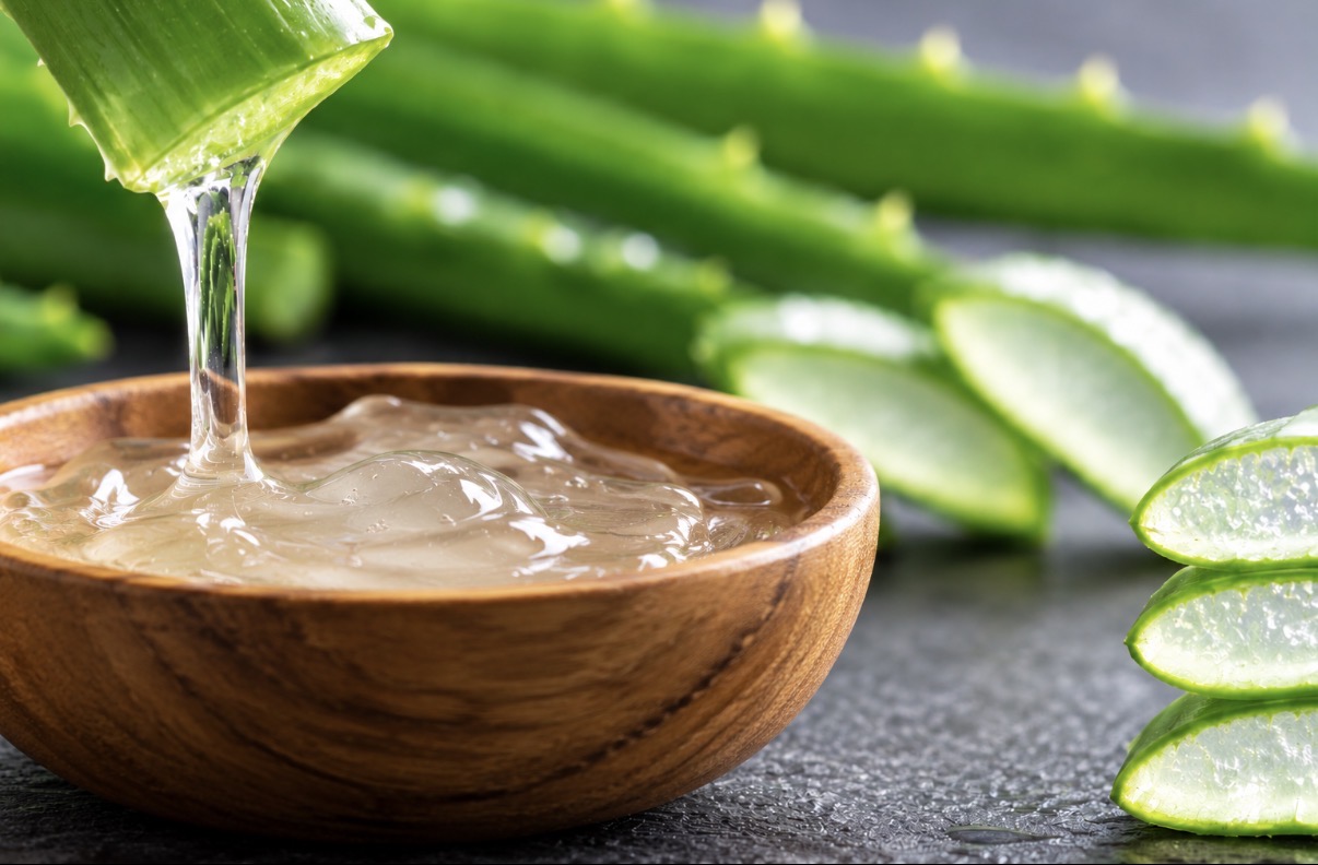 Gel d’aloe vera versé depuis une feuille coupée dans un bol en bois, à côté de tranches de feuilles d’aloe vera